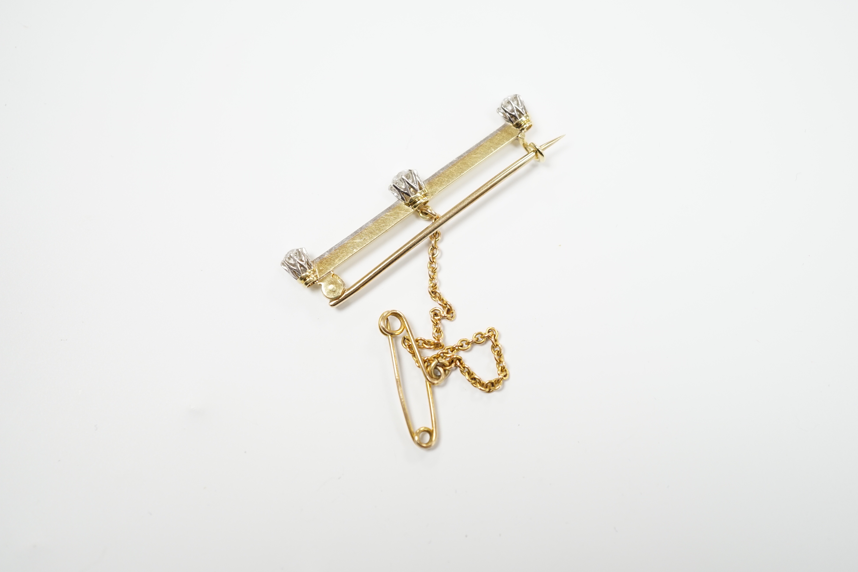 A yellow metal and three stone diamond set bar brooch, 37mm, with safety chain, gross weight 3 grams.